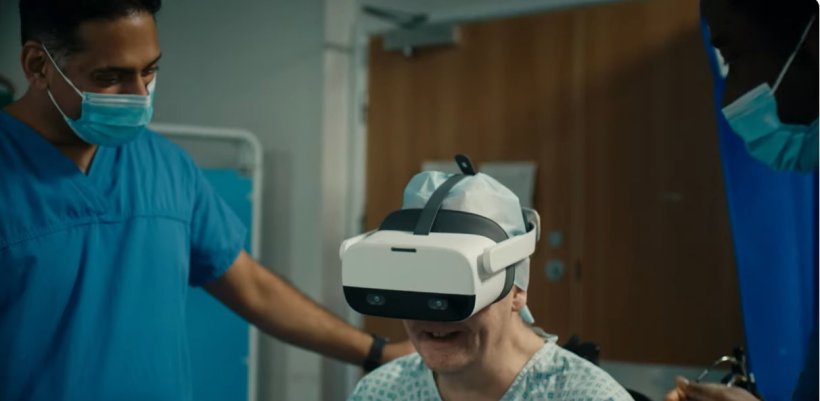 A patient wearing a VR headset and a medical gown is monitored by surgeons...