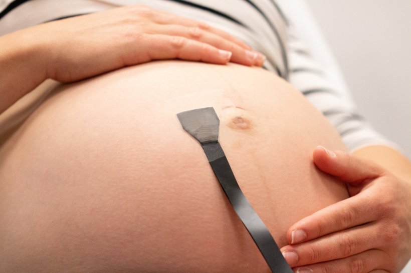 Cropped photo of a pregnant womans belly, with a small sensor attached close to...