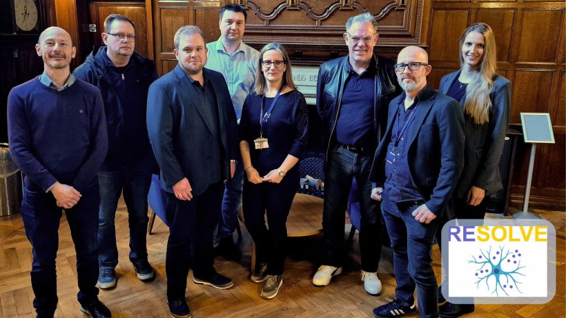 Ein Gruppenfoto mit acht Personen in einem Raum mit Fischgräten-Parkett und...
