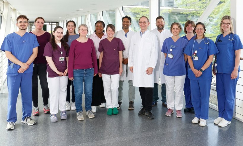 Gruppenfoto mit 14 Personen, die nebeneinander im verglasten Flur eines...