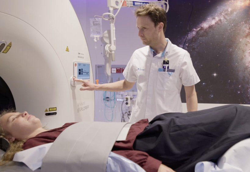 A woman is undergoing a medical scan in a PET/CT scanner. Next to the patient...