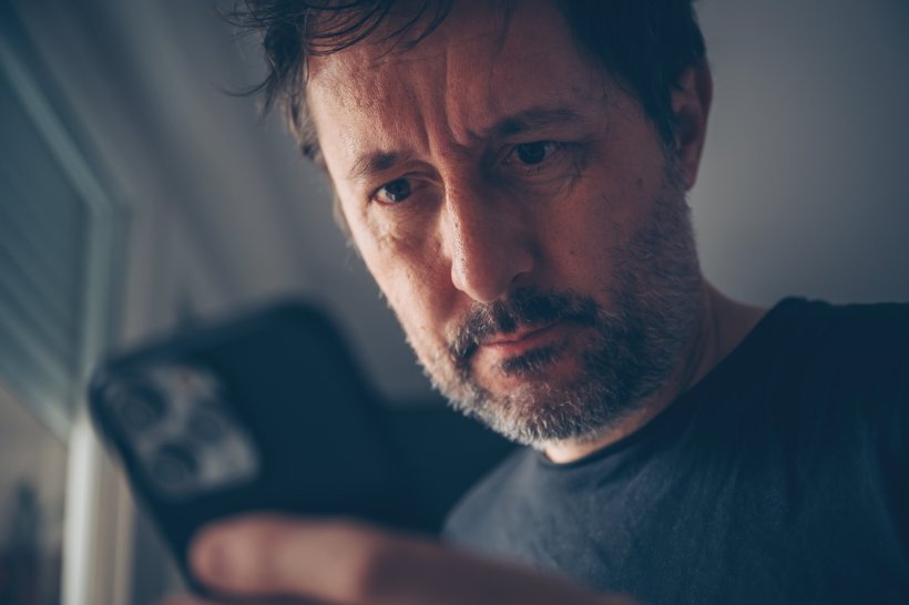 A man with a concerned expression is looking at his smartphone