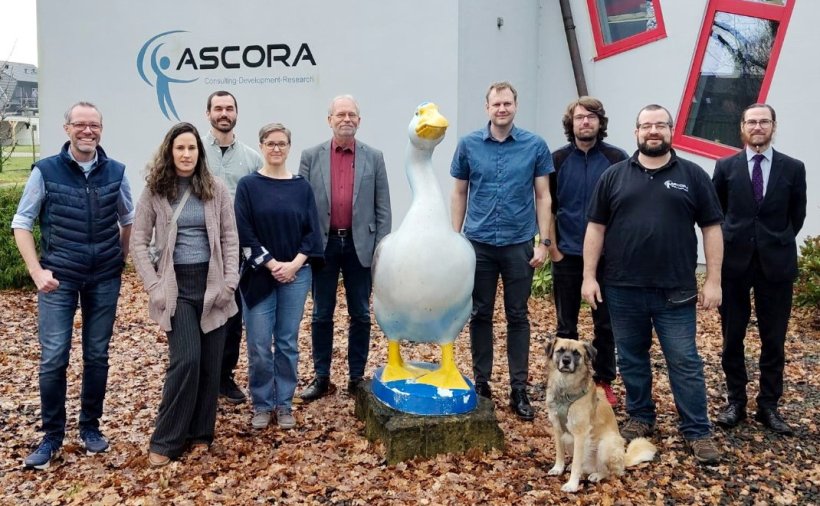 Ein Gruppenfoto mit neun Personen und einem Hund, die draußen vor einem...