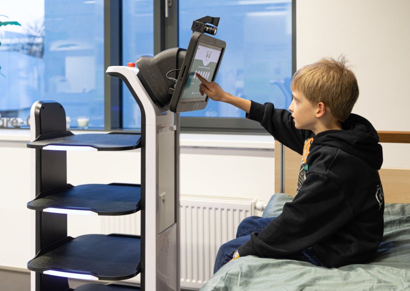 Ein Kind sitzt auf einem Krankenhausbett und bedient den Touchscreen eines...