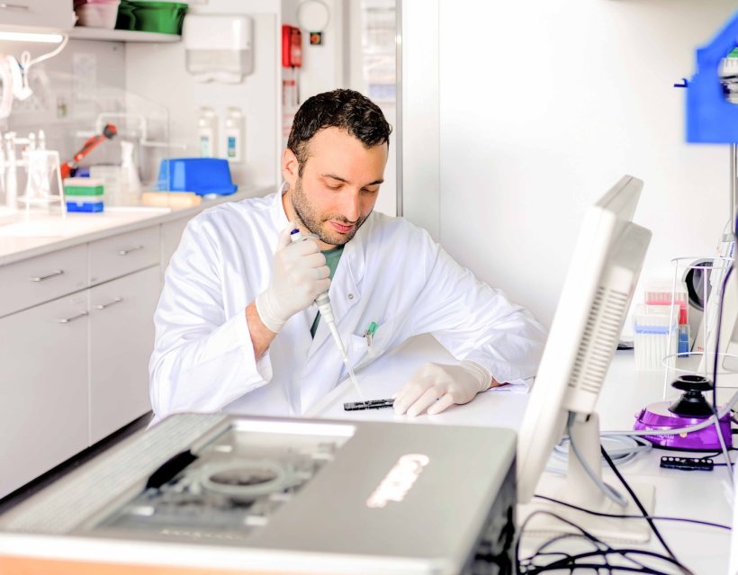 Dr. Micha Banz sitzt an einem Arbeitsplatz im Labor und benutzt eine Pipette