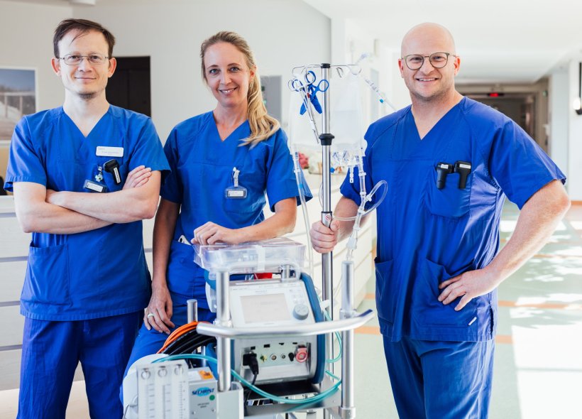 Drei Mediziner im blauen Kasack stehen im Flur eines Krankenhauses um ein...