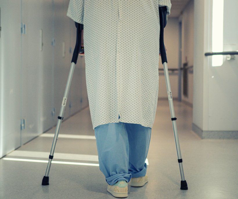 A person wearing a hospital gown is moving along a hospital coridor with the...
