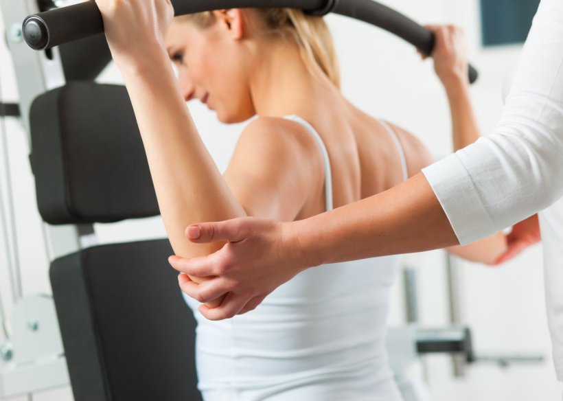 Eine junge Frau bedient bei der Physiotherapie ein Trainingsgerät zur...