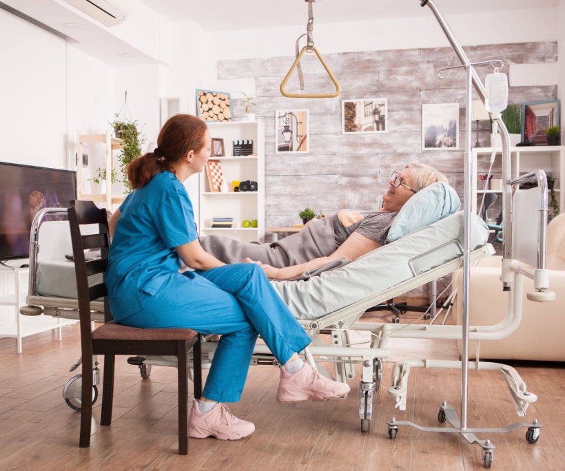 A healthcare professional is sitting next to a patient bed with an older woman...