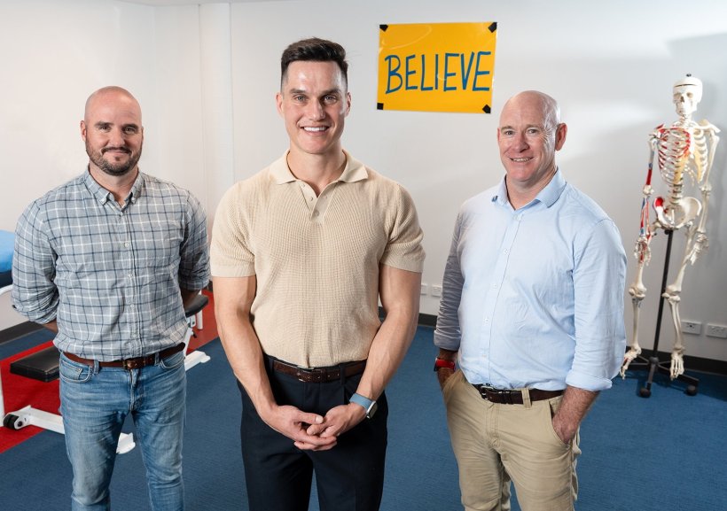 Three men are standing in a room with a medical patient rest, anatomical...