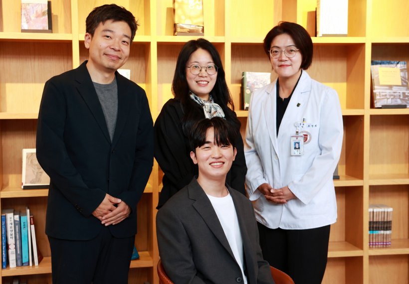 Four people standing and sitting in front of a tidy bookshelf for a team photo
