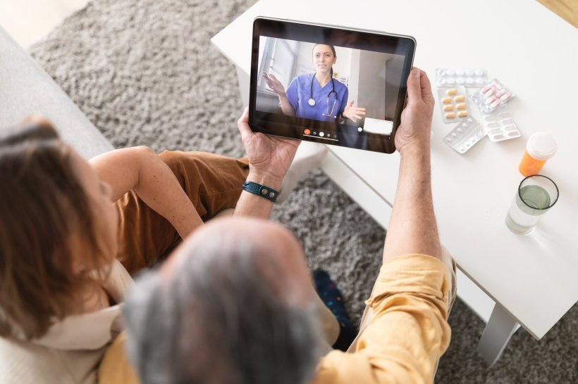 Two people on a sofa are using a tablet device for medical teleconsultation. On...