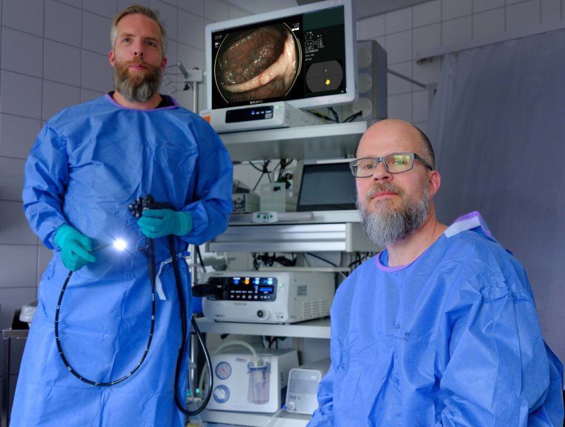 Zwei Mediziner in blauen Schutzkitteln stehen und sitzen um ein...
