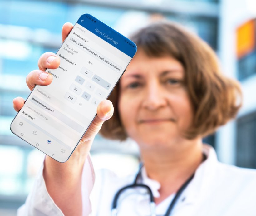 Eine Ärztin mit weißem Arztkittel und Stethoskop hält ein Smartphone mit...