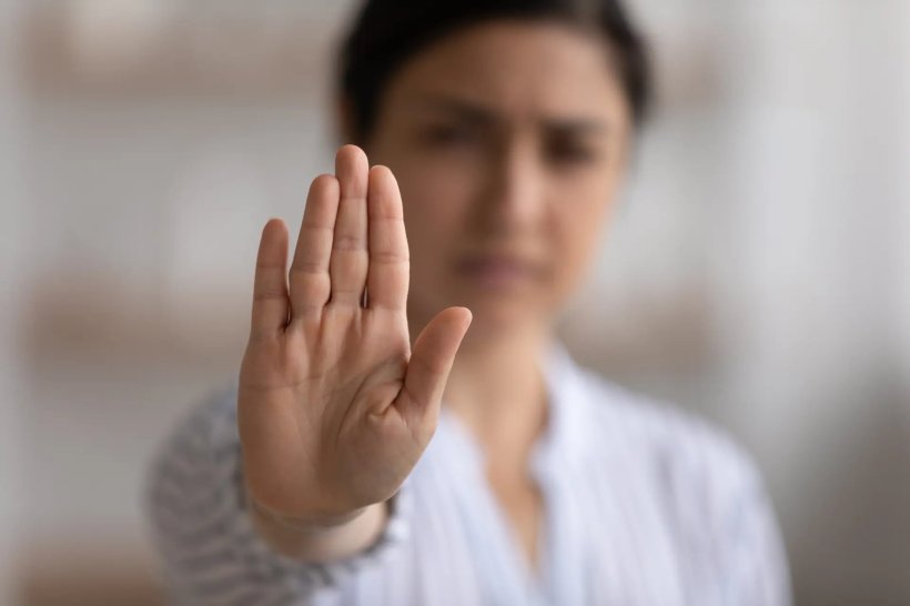 Eine Frau hält in einer Stop-Geste ihre rechte Handfläche in die Kamera. Der...