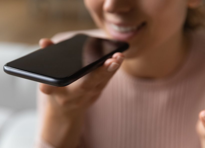 Eine Frau spricht in das Mikrofon ihres Smartphones. Sie hält das Telefon...