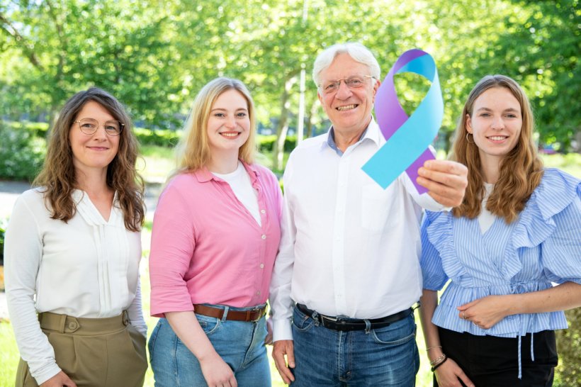 Vier Personen stehen für ein Teamfoto nebeneinander in einem Außengelände,...