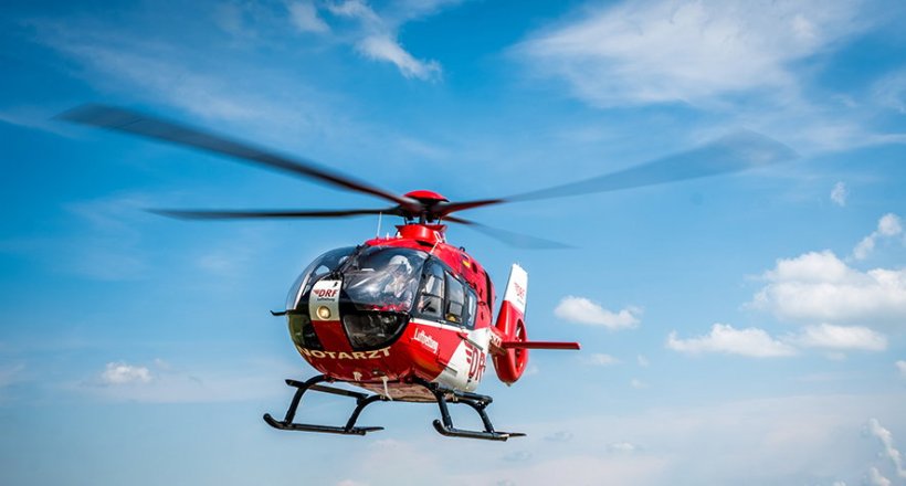 Ein roter Rettungshubschrauber in der Luft vor einem blauen Himmel mit leichter...