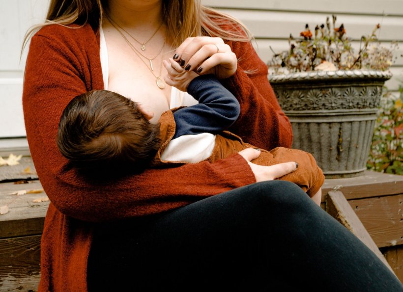 A mother is sitting outside, breastfeeding her baby