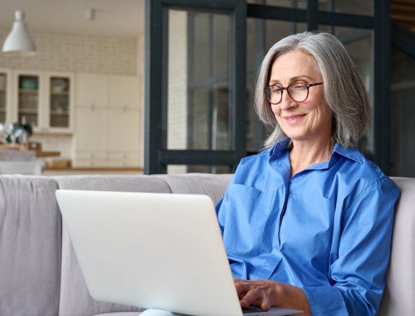 A smiling woman is using her laptop computer while sitting on a sofa
