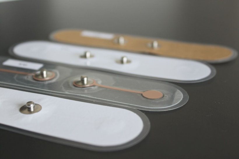 Vier Elektroden aus Papier liegen auf einer grauen Unterlage