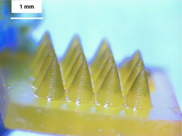 Closeup photo of a minuscule yellow plate with tiny spikes (microneedles),...