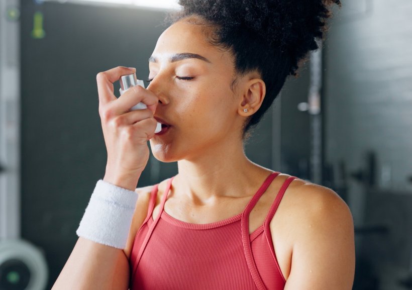 A young woman is using an inhaler for asthma and COPD treatment in a gym...