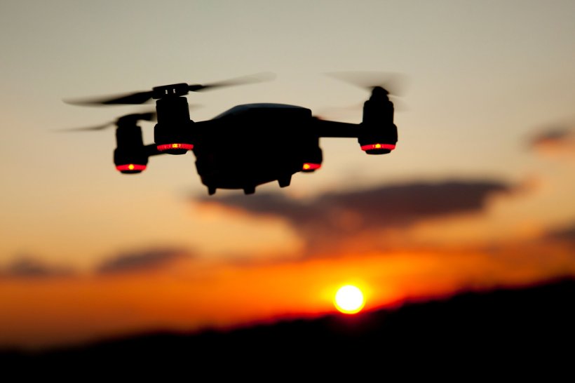 A quadcopter drone is flying in a sunset sky