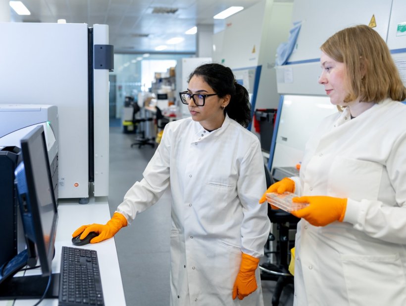 Two scientists wearing lab coats and orange gloves observe tuberculosis test...