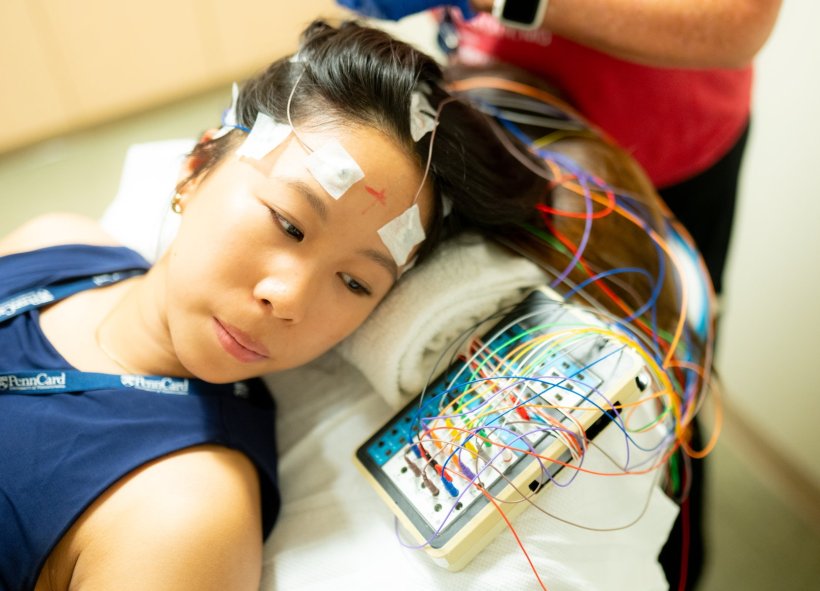 A woman is lying on a patient rest, with electrodes connected to her head. The...