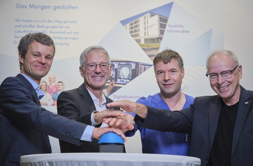Vier Personen stehen an einem Stehtisch und drücken gemeinsam auf einen blauen...