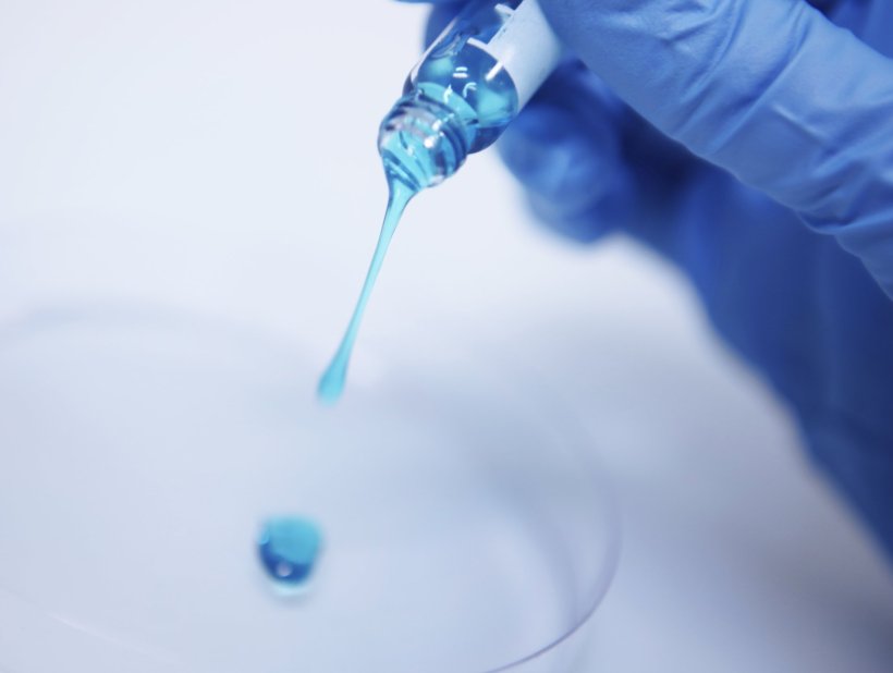 Closeup photo of a hand in a blue rubber glove dripping a drop of blue liquid...