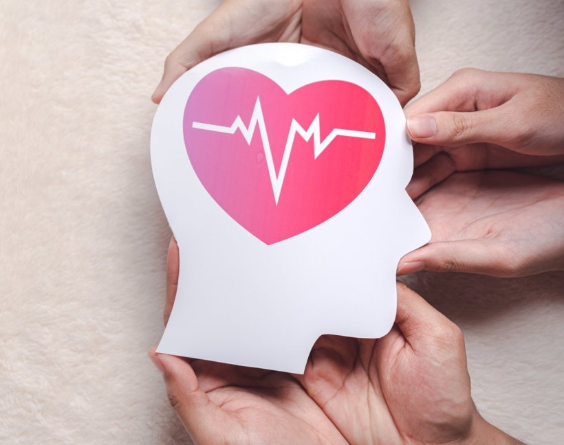 Three pairs of hands are holding a paper silhouette of a head, with a heart...
