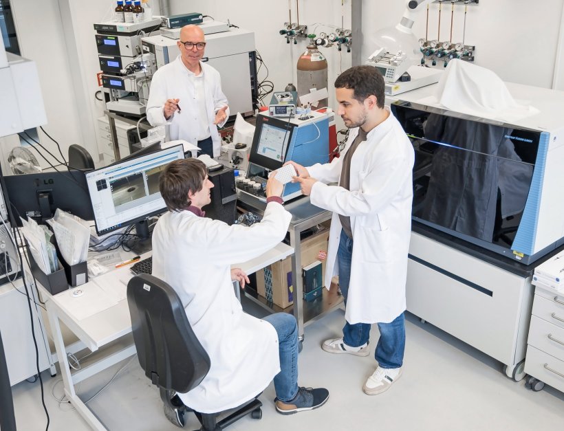 Drei Wissenschaftler in weißen Laborkitteln in einem medizinischen Labor mit...