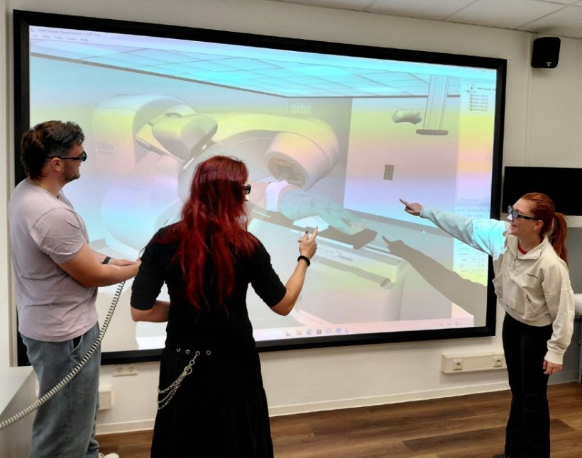 Drei Personen stehen vor einer großen Projektion, die eine 3D-Simulation einer...