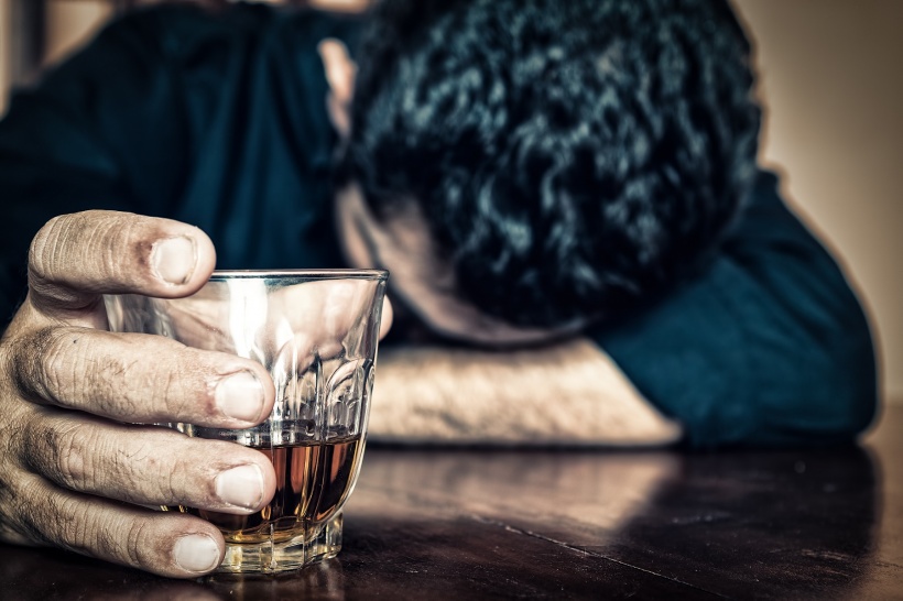 Depressed drunk man holding a drink and sleeping with his head on the table