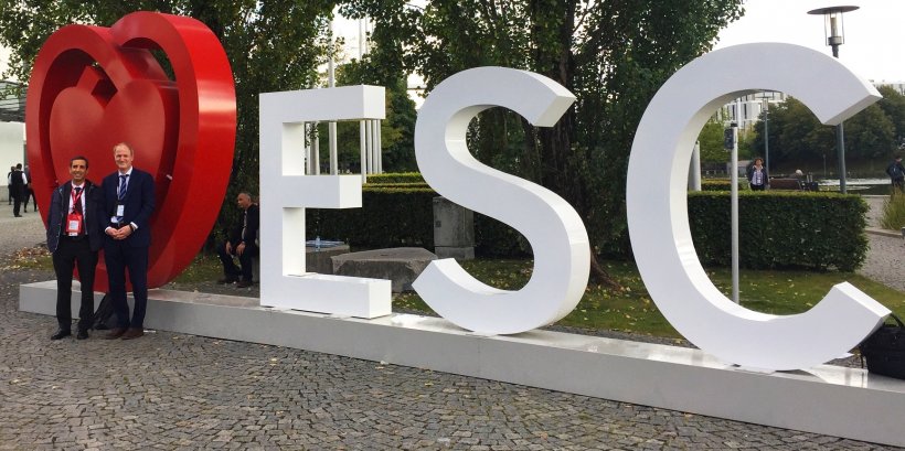 two men in suits standing in front of the esc cardiology congress logo