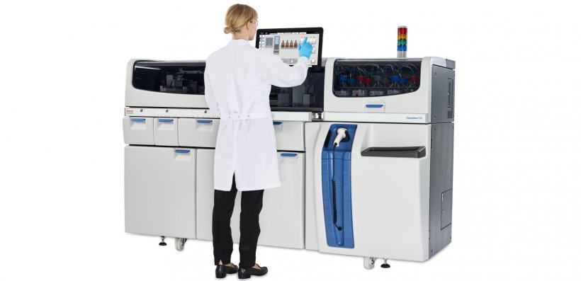 woman in a lab coat standing in front of a clinical analyzer