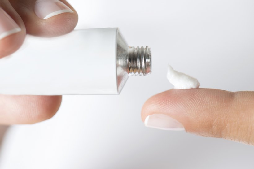 female hands applying skin cream from a white tube