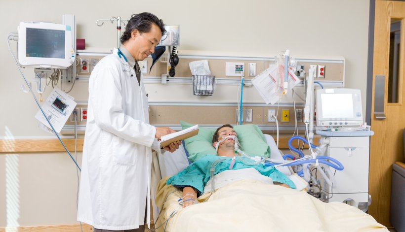 Mid adult doctor with clipboard examining patients report in hospital room