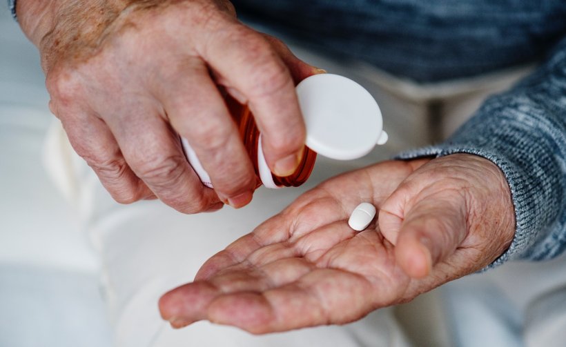 hands of elderly man with pill bottle and white pills