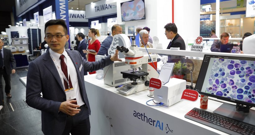 joe yeh at aetherAI booth at medica 2019. a microscope is connected to a...