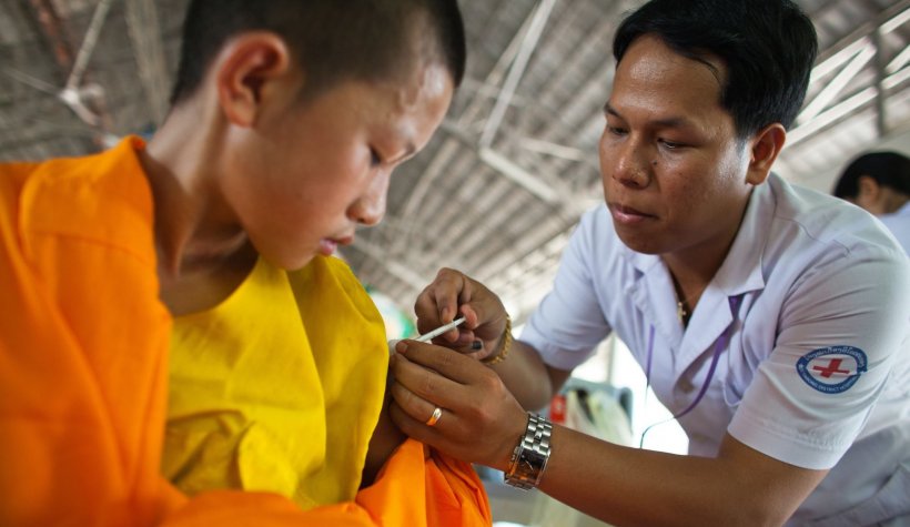 boy in orange clothing receiving vaccine from vietnamese red cross medical staff