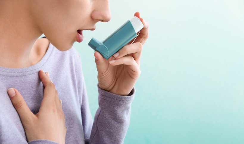 Young woman using inhaler against asthma