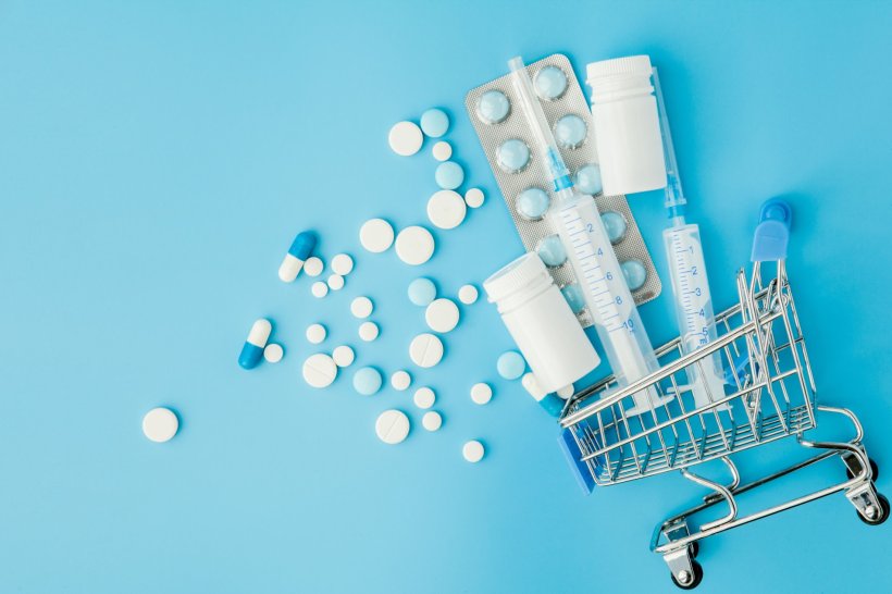 shopping cart filled with medical equipment, pills and syringes, on blue...