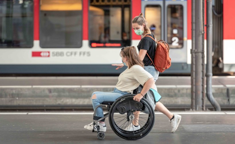 woman in wheelchair and another woman walking across train station platform