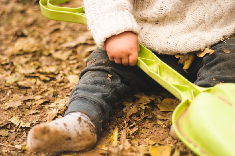 young toddler playing in the dirt with green plastic shovel