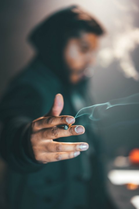 man out of focus holding a marihuana cigarette in his hand