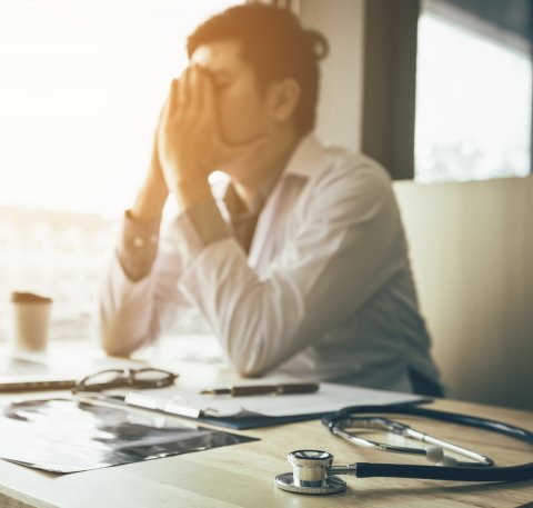 physician holding his face in his hands, showing singsn of burnout