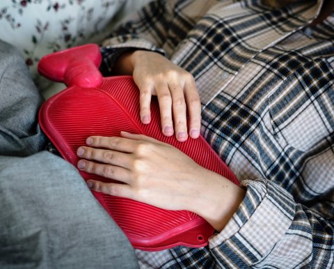 woman with abdominal pain holding a red hot-water bottle
